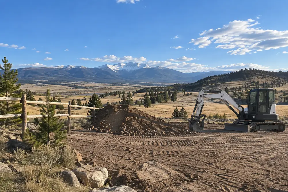 Graded acreage homesite on open ranchland with a mini excavator and a wooden fence