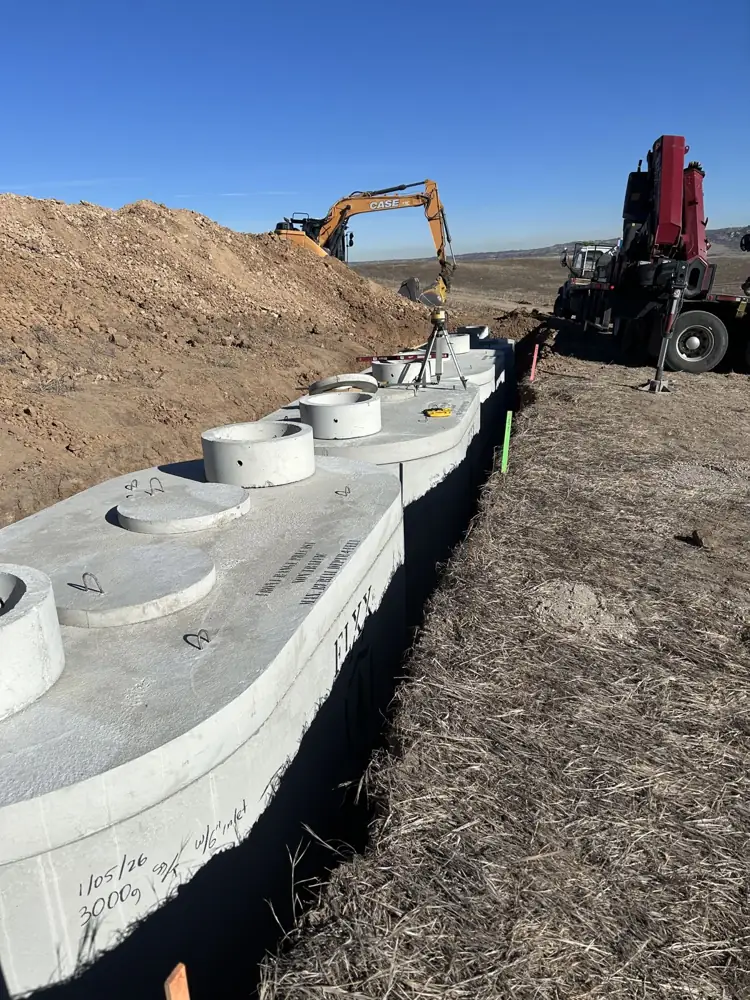 Row of concrete septic tank sections set in a trench with equipment behind