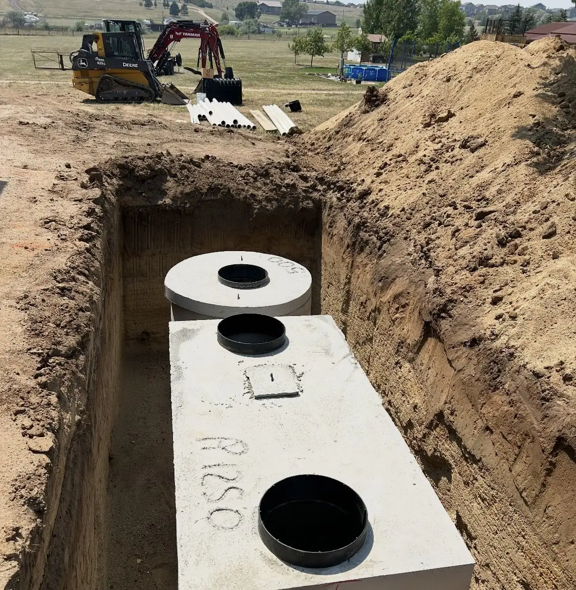 Concrete septic tank set in an excavated trench with a tracked machine working nearby